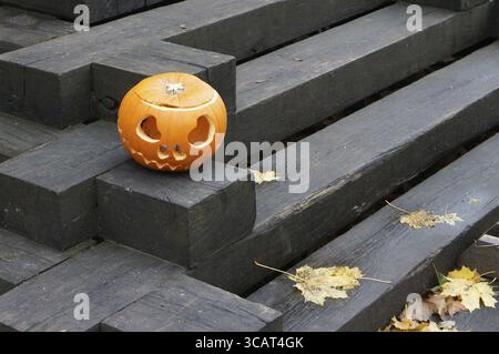 Citrouille sculptée avec les yeux et la bouche sur un escalier en bois noir. Matin Après Fêtes Halloween Banque D'Images