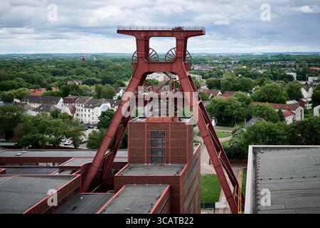Vue aérienne d'une structure industrielle rouge ressemblant à une tour minière, entourée d'arbres verts et de bâtiments résidentiels sous un ciel nuageux. Banque D'Images