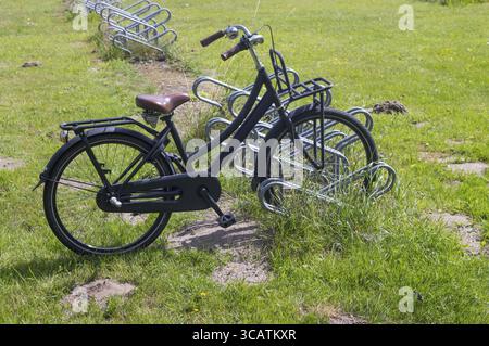 Vélo néerlandais noir classique avec siège en cuir marron et guidon appuyés sur un support de stationnement de vélo en métal vide par une journée d'été ensoleillée Banque D'Images