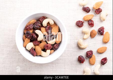 Mélange sentier canneberge amande cajou, dans un bol blanc, sur lin. Canneberges sucrées séchées, avec des amandes crues et des noix de cajou. Collation populaire. Banque D'Images