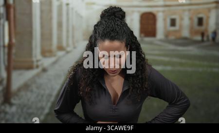 Femme debout à l'extérieur dans une université historique avec un regard d'inconfort sur son visage soulignant l'architecture ancienne et le chemin pavé. Banque D'Images