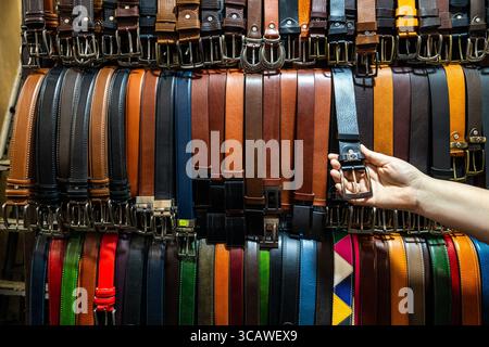 Une main de client qui choisit une ceinture en cuir dans un étal coloré du marché au Mercato Nuovo à Florence, en Italie Banque D'Images