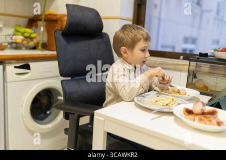 Garçon mangeant le déjeuner et regardant la tablette dans la cuisine Banque D'Images