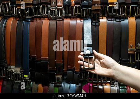 Un client ramasse une ceinture en cuir sur un stand de marché au Mercato Nuovo à Florence, en Italie Banque D'Images