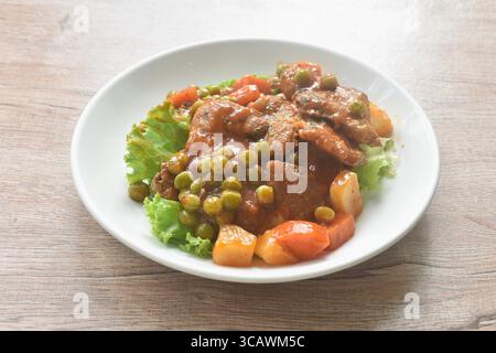 steak de porc braisé dans un ragoût de sauce sauce avec garniture de légumes laitue fraîche sur l'assiette Banque D'Images