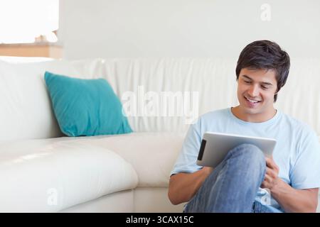 Homme assis, appuyé contre le canapé avec oreiller sarcelle, en utilisant la tablette dans le salon lumineux, espace de copie Banque D'Images
