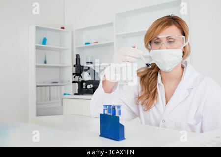 Tube à essai maintenu à hauteur des yeux au-dessus de la paillasse de laboratoire avec le portoir bleu à côté du microscope noir Banque D'Images