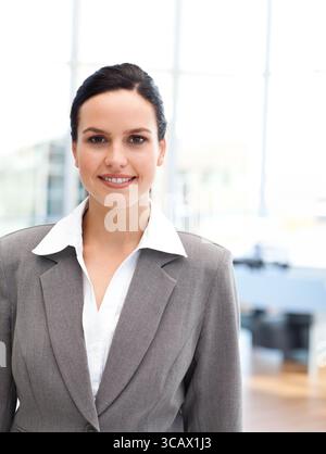 Femme professionnelle portant un blazer sur mesure, debout dans un bureau moderne avec des baies vitrées Banque D'Images