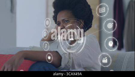 Femme mi-adulte penchée s'engageant avec des superpositions numériques sur le canapé dans le salon, avec coussin rouge Banque D'Images