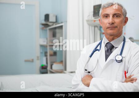 Médecin masculin principal debout à côté de la table d'examen dans la salle d'examen de l'hôpital avec stéthoscope, espace de copie Banque D'Images