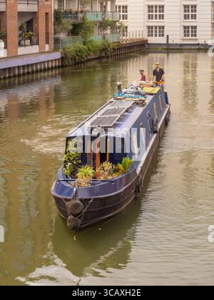 Deux personnes sur un bateau étroit traditionnel, une vue commune sur le Regent's canal qui traverse Camden et d'autres parties de Londres, Royaume-Uni. Banque D'Images