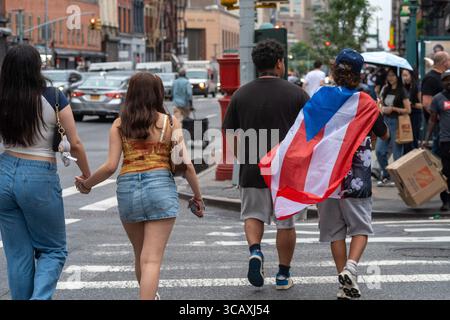 Groupe de jeunes se promène dans la rue animée de la ville, l'un drapé dans une cape de drapeau, incarnant le dynamisme urbain et la diversité. Banque D'Images
