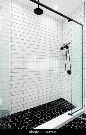 Une douche avec des murs de carrelage blanc de métro, un sol en carrelage hexagonal noir et des pommes de douche noires. Banque D'Images