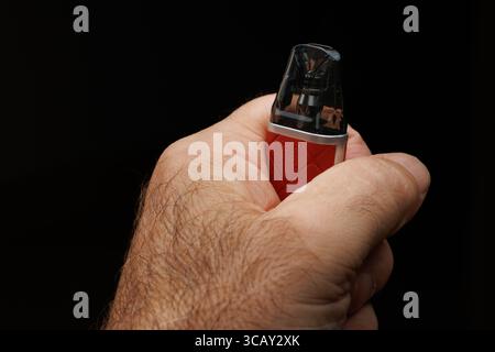 Main de personne méconnaissable tenant cigarette électronique sur fond noir Banque D'Images