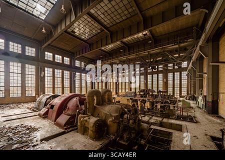 Vue intérieure d'une centrale électrique industrielle abandonnée avec de grandes machines et de la lumière naturelle coulant à travers de hautes fenêtres Banque D'Images