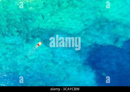 Vue aérienne drone d'homme nageur avec des malles de natation rouges dans l'eau turquoise. Mer Ionienne, île de Céphalonie, Grèce Banque D'Images