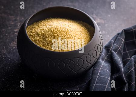 Couscous cru dans un bol sur une table noire. Banque D'Images