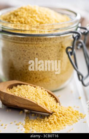Couscous cru dans une pelle en bois sur une table blanche. Banque D'Images