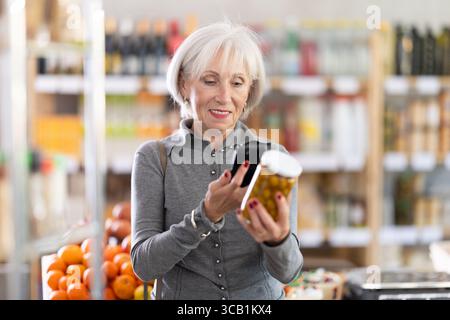 Femme âgée scannant le code qr pour les olives Banque D'Images