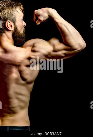 Un homme musclé fléchit son biceps, mettant en valeur son physique sur un fond noir. Banque D'Images