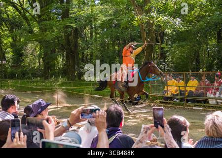 Exposition de tir à l'arc traditionnel japonais à cheval pendant le festival Yabusame Shinji, mettant en vedette un archer qualifié visant à mi-parcours, observé par un ingénieur Banque D'Images