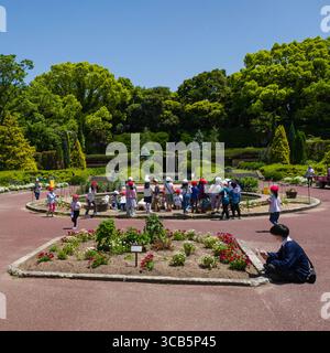 Un groupe d'enfants explore un parc de jardin animé, entouré d'une végétation luxuriante et de fleurs colorées sous un ciel bleu clair Banque D'Images
