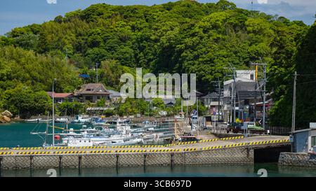 Une vue panoramique sur un port de village côtier tranquille avec des bateaux et des collines verdoyantes sous un ciel ensoleillé, Sasebo, Japon Banque D'Images