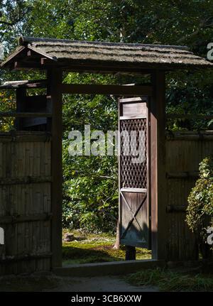 Portail en bois avec un toit de chaume magnifiquement vieilli entouré d'une végétation luxuriante et d'arbres vibrants sous la lumière du jour. Temple de Shisendō, Kyoto Banque D'Images