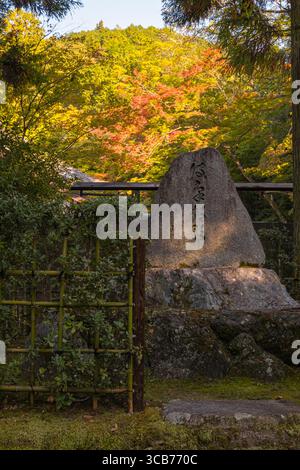Scène de jardin japonais avec un monument en pierre, une clôture en bambou et un feuillage d'automne vibrant sous la lumière douce du soleil, Kyoto, Japon Banque D'Images