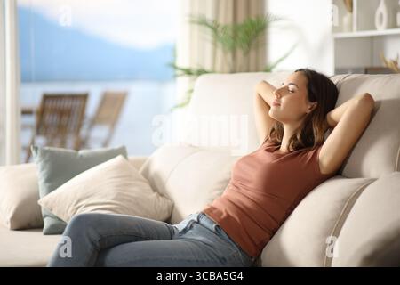 Femme célibataire détendue se reposant sur un canapé à la maison à côté d'une fenêtre Banque D'Images
