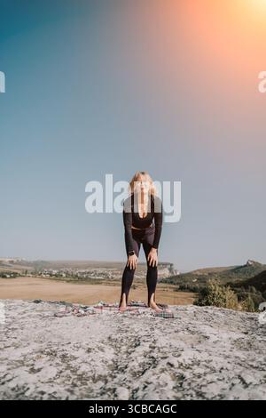 Jeune femme s'étirant sur un sommet de montagne Banque D'Images