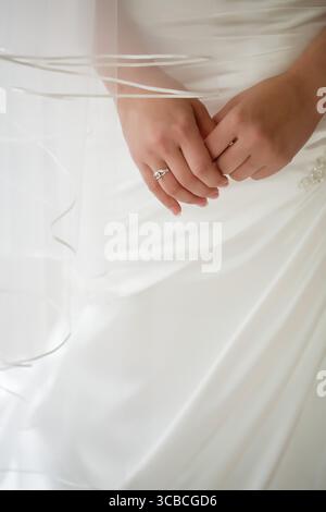 Les mains de la mariée se sont serrées au-dessus de l'anneau de présentation de robe blanche coulante. Banque D'Images