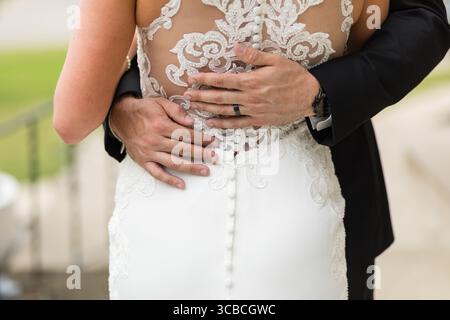 Le marié embrasse la mariée par derrière, avec des boutons de robe à dentelle arrière Banque D'Images