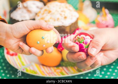 Tradition familiale de Pâques. Fille et mère battant des œufs de Pâques contre Kulich ou gâteau de pâques Banque D'Images