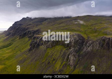 Nuages embrassant des falaises accidentées et des pentes verdoyantes en islande Banque D'Images