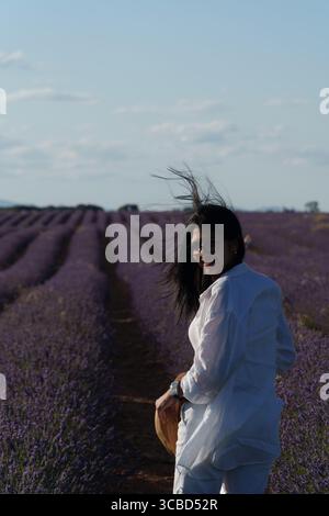 Une femme debout dans un champ de lavande. Elle porte une chemise blanche et un chapeau de paille Banque D'Images