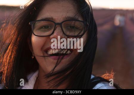 Une femme aux cheveux longs et aux lunettes sourit. Elle porte une chemise blanche. La femme est debout dans un champ Banque D'Images
