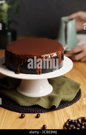 Tranchant à la main un riche cheesecake à la croûte foncée, avec des couches crémeuses de vanille et de chocolat, surmonté de ganache au chocolat brillant. Banque D'Images