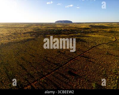 Vue aérienne du monolithe emblématique d'Uluru s'élève majestueusement du sol du désert ocre-rouge sous le vaste ciel Azur, Petermann, Northern Territor Banque D'Images