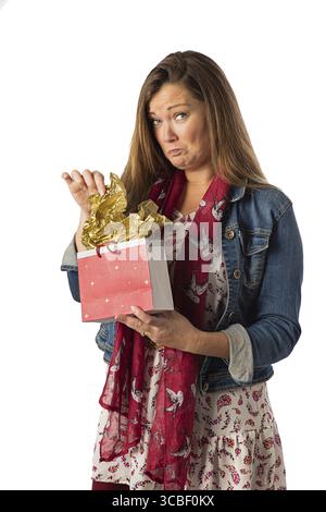Femme de quarante ans, portant des vêtements de style bohème, ouvrant un sac cadeau, avec une expression malheureuse, isolée sur un fond blanc Banque D'Images