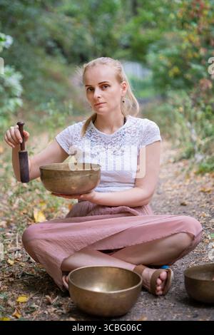 Jeune femme en séance de guérison sonore dans la nature avec des bols chantants tibétains. Banque D'Images