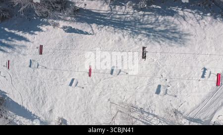 Vue aérienne d'une remontée mécanique transportant les skieurs sur une pente enneigée par une journée ensoleillée, offrant une vue imprenable sur les sports d'hiver et les loisirs. Station de ski de Bukovel. Fond de voyage de nature hivernale Banque D'Images