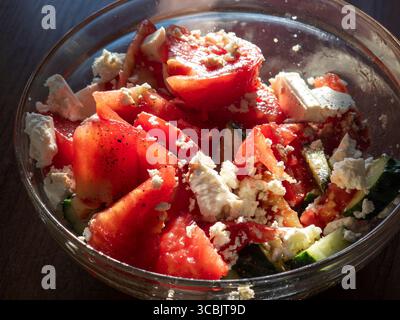Les tomates et les concombres tranchés sont combinés avec du fromage feta émietté, créant une salade d'été simple mais rafraîchissante, servie dans un bol en verre et assaisonnée Banque D'Images