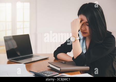 Jeune architecte asiatique tenant le front tout en travaillant sur le projet au bureau. Elle est fatiguée et fatiguée. Banque D'Images