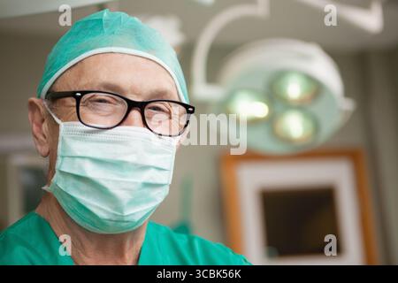Chirurgien portant un équipement chirurgical vert et des lunettes à cadre noir travaillant sous la lampe à l'aide d'un moniteur dans OU. Médical, santé, professionnalisme, clinique, préc Banque D'Images