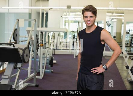 Homme debout près de la presse à jambes et des barbillons dans le gymnase contre des murs en miroir vérifiant la montre de sport. Fitness, force, entraînement, entraînement, athlétique, santé, Banque D'Images