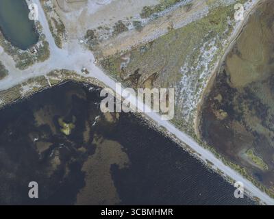 Vue aérienne du contraste saisissant entre les eaux sombres et la terre pâle et texturée, divisée par de minces sentiers, Gruissan, Occitanie, France. Banque D'Images