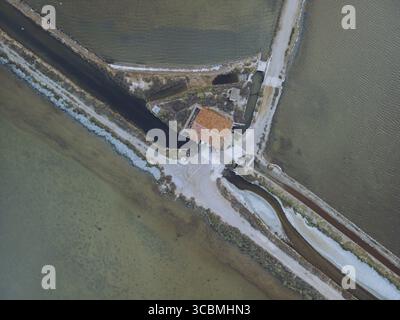 Vue aérienne de marais salants géométriques entrecoupés par des canaux étroits, créant une mosaïque de tons terreux, près d'une pittoresque structure à toit rouge, Gruissan, O. Banque D'Images
