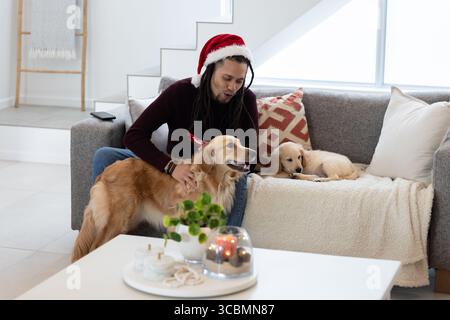 Homme adulte moyen portant chapeau de Père Noël caressant chien Golden retriever comme chiot couché dans le salon. Confortable, moderne, intérieur, compagnie, détente, accueil, l Banque D'Images