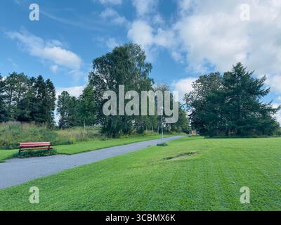 Vue panoramique sur le parc par une journée ensoleillée avec un chemin, de l'herbe verte, des arbres et un ciel nuageux à Jämtland, Suède. Banque D'Images